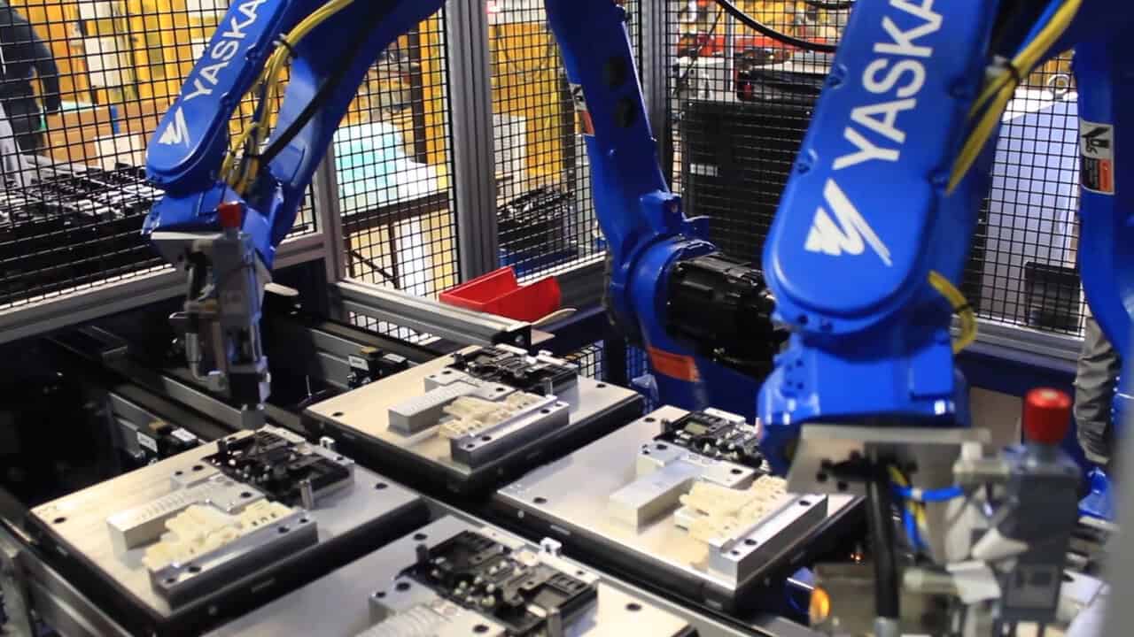 Two Yaskawa-Motoman blue robots performing assembly tasks on a pallet line